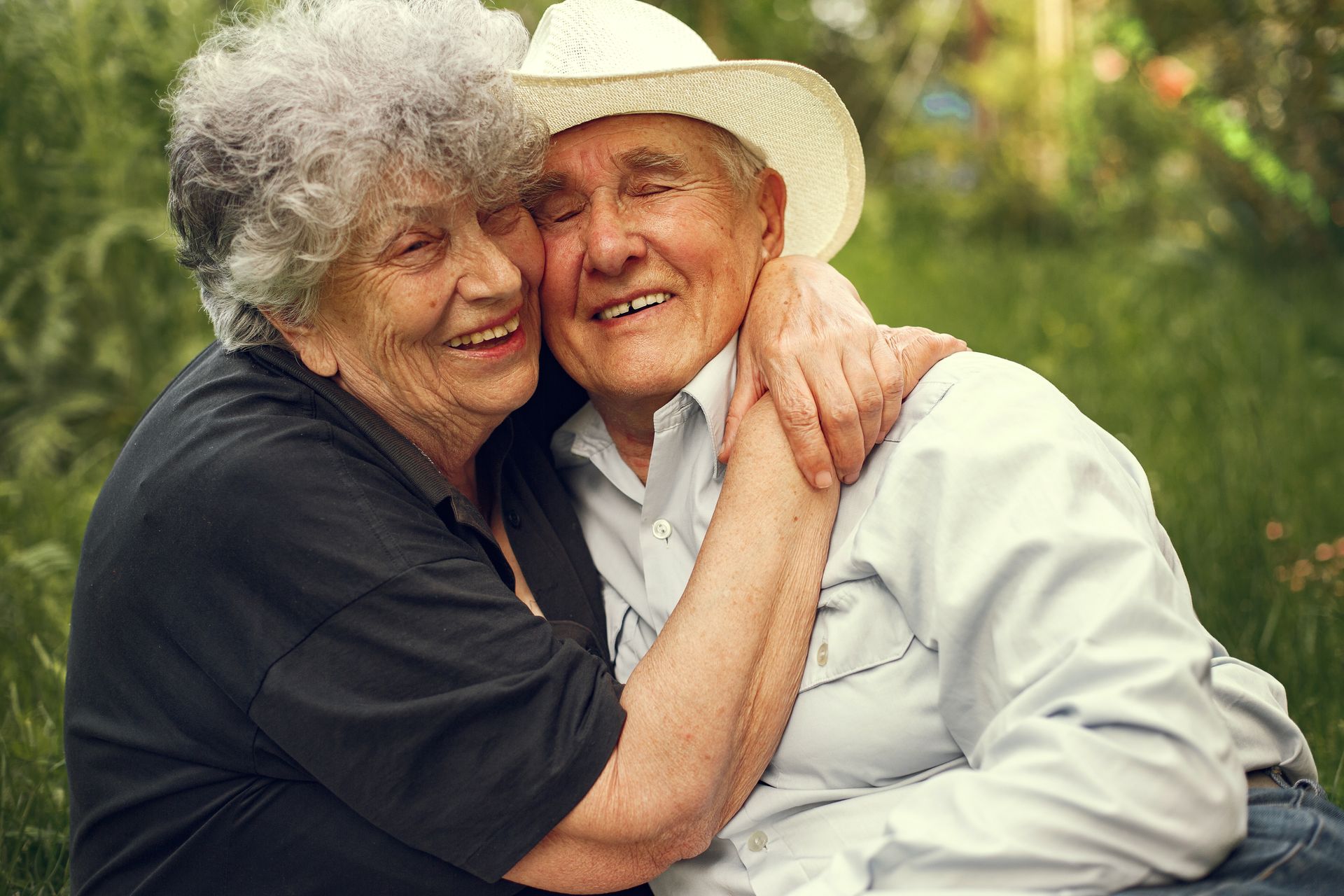 We zien een mevrouw en meneer op leeftijd in de tuin. Ze lachen en de vrouw omhelst de man.